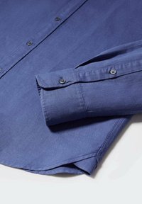 Camicia blu navy con bottoni, caratterizzata da una texture liscia, maniche lunghe con polsini abbottonati e orlo curvo.