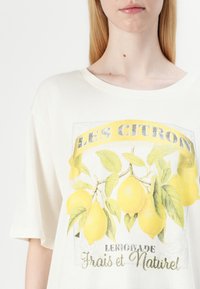 T-shirt blanc à manches courtes avec un graphique de citron, des feuilles vertes et le texte "LES CITRON" et "Limonade Frais et Naturel" en argent.