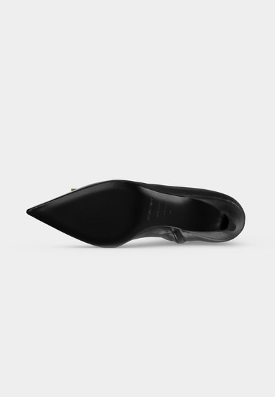 Chaussure stiletto noire à bout pointu, vue de la semelle avec une finition lisse et brillante sur un fond clair uni.