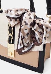 Sac fourre-tout avec panneaux beiges, crème et noirs, fermoir chaîne dorée, et foulard en soie noué avec un motif tacheté marron et blanc.