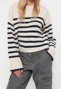 Pull tricot à rayures crème et marine avec manches longues, encolure ronde et poignets côtelés, assorti à un pantalon cargo gris.