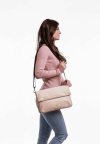 Béžová syntetická taška přes rameno s klopou, která má dlouhý nastavitelný popruh a minimalistický design, vystavená na bílém pozadí.