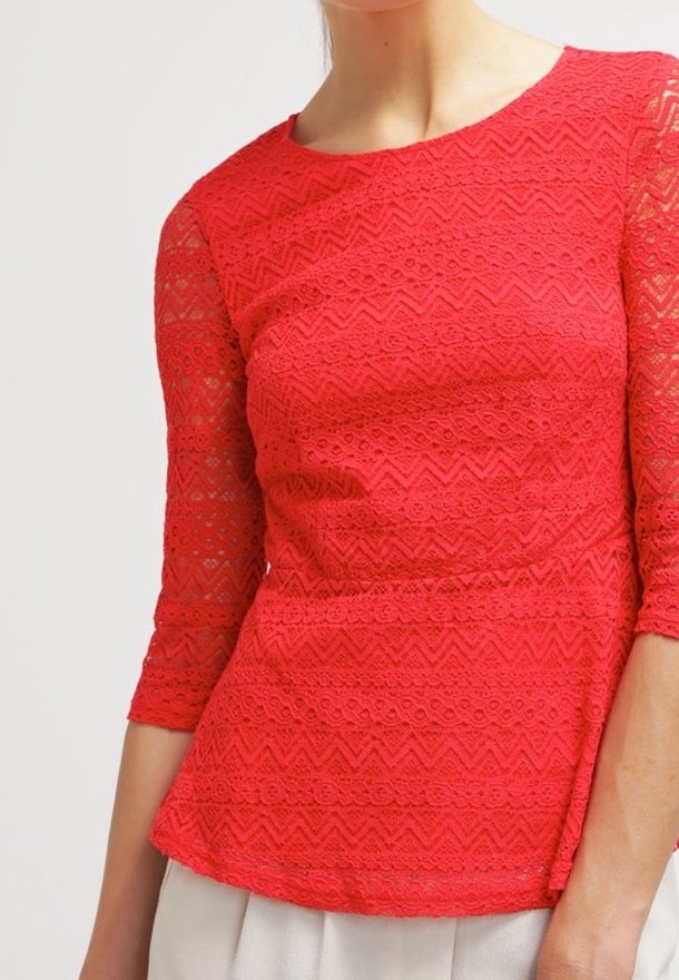Top en dentelle rouge avec des manches trois-quarts, présentant un motif zigzag texturé et un ourlet peplum. Design léger et ajusté.