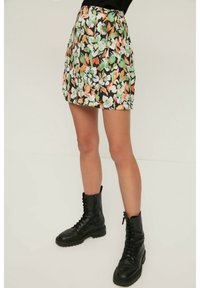 Jupe mini florale avec un fond noir et des fleurs orange, vertes et blanches. Fabriquée en tissu léger, elle est conçue avec une taille haute.