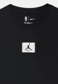 Črna bombažna majica z okroglim izrezom, na kateri je bel našitek z vezenim logotipom Jumpman in napisom "Flight" spodaj. Notranjost ovratnika ima označbe Nike in NBA.