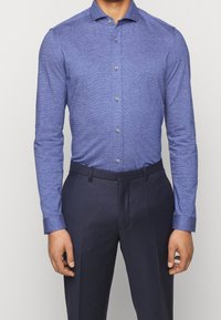 Blauw langlijnig overhemd in een textuurrijk stof, met een button-down kraag en knopen aan de voorkant, gecombineerd met donkere broek.