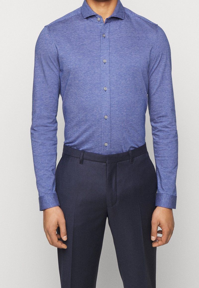 Blauw langlijnig overhemd in een textuurrijk stof, met een button-down kraag en knopen aan de voorkant, gecombineerd met donkere broek.