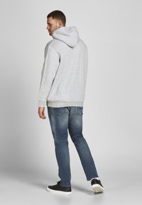Grijze hoodie met een kangoeroe zak en een capuchon met koord, gecombineerd met middelblauwe jeans en zwarte sneakers. Glad textuur van de stof.