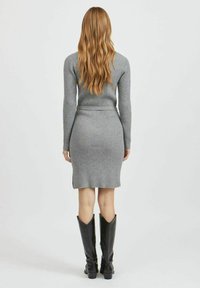 Abito a maglia grigio a coste con maniche lunghe, silhouette aderente e spacco laterale, abbinato a stivali in pelle nera al ginocchio.