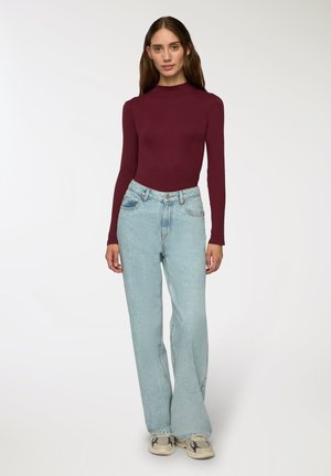 Maglietta bordeaux a maniche lunghe con collo alto abbinata a jeans chiari a vita alta e gamba larga e scarpe da ginnastica con fantasia.
