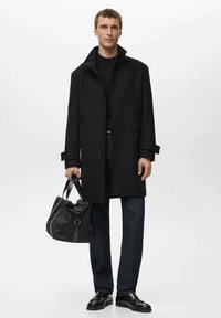 Czarny wełniany płaszcz z wysokim kołnierzem, zapinany na guziki z dwoma kieszeniami. W połączeniu z czarną torbą, ciemnymi dżinsami i czarnymi eleganckimi butami.