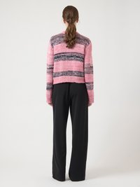 Pink knitted sweater with dark stripes, cropped design, textured fabric, paired with black wide-leg pants. Visible ribbed cuffs and hem.