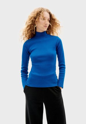 Blaues, geripptes Rollkragenoberteil mit langen Ärmeln, taillierte Passform, glatte Textur, kombiniert mit lockeren schwarzen Hosen.