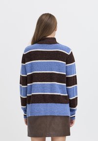 Maglione a righe lavorato a maglia nei colori marrone, blu e bianco. Presenta un colletto alto e una vestibilità ampia. Tessuto texture con polsini a costine.