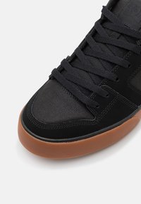 Fekete sneaker textúrált szövet felsőrésszel, lapos fekete cipőfűzőkkel és gumírozott talppal. Lekerekített orr rész díszítő varrásokkal.