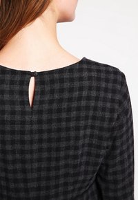 Top z czarno-szarym wzorem w kratę, z zaokrąglonym dekoltem, otworem typu keyhole z tyłu i z pojedynczym zapięciem na guzik.