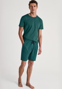 Teal t-shirt met korte mouwen en bijpassende shorts met een elastische tailleband. De stof is glad en de shorts hebben twee zijzakken.