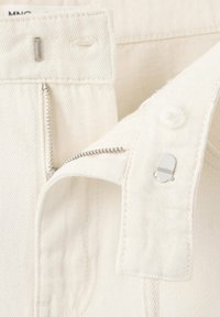 Gros plan sur un pantalon en denim blanc avec une fermeture éclair argentée ouverte, un crochet en métal, un boutonnière et un bouton sur la ceinture.