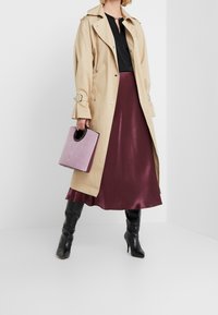 Beżowy trencz z srebrnymi guzikami, czarna bluzka i bordowa satynowa spódnica. Czarne kozaki za kolano oraz lawendowa torebka w kształcie pudełka z okrągłym uchwytem.