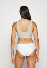 Beige avskåret topp med vid halsutskjæring og tykke stropper, sammen med hvite høytgående undertøy. Glatt tekstur, minimalistisk design.