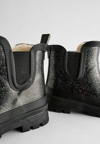 Bottes de cheville noires brillantes avec des paillettes scintillantes, des panneaux latéraux texturés et un intérieur doux doublé de fourrure. Semelle en caoutchouc avec des rainures pour l'adhérence.