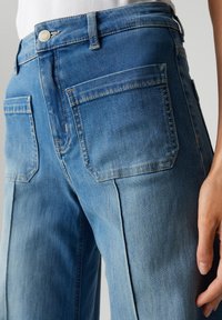 Jean en denim bleu clair avec une coupe droite, comprenant deux poches arrière et des effets de décoloration subtils sur le tissu.