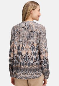 Bluzka z długim rękawem z lekkiego materiału, zdobiona skomplikowanymi wzorami paisley i diamentami w odcieniach szarości, beżu i brzoskwini. Zapięcie na guziki z tyłu.