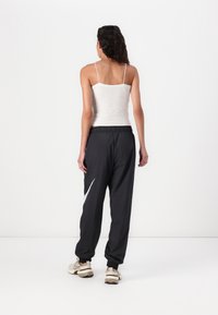 Czarne dresowe spodnie z elastycznym pasem, zdobione białym ukośnym paskiem, zestawione z jasnoszarym topem na ramiączkach i beżowymi tenisówkami.