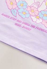 Fliederfarbenes Baumwoll-T-Shirt mit floralem Druck in Pink und Blau. Der Text lautet: "Immer anhalten und die Blumen riechen, Miss Bunny."