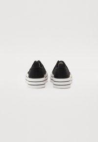 Sneakers di tela nera con design piatto, suola in gomma rigata bianca e linguetta sul retro per una facile calzata.