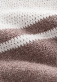 Pletená látka s cikcak vzorom striedajúcim sa v bielych a svetlohnedých pruhoch. Mäkká textúra s viditeľnými vláknami po celej ploche.