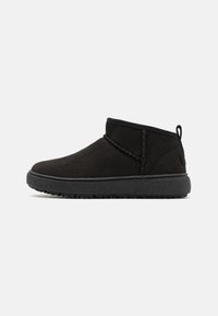 Botines de ante negros con punta redondeada, detalles de costura y suela de goma texturada. Cuenta con una tira en la parte posterior para ponerse con facilidad.