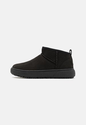 Bottines en suédine noire avec un bout arrondi, des détails cousus et une semelle en caoutchouc texturé. Équipées d'une languette à l'arrière pour un enfilage facile.