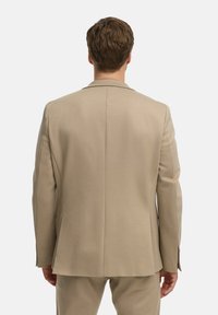 Beige Maßanzugjacke mit einem Schlitz, mit Schalkragen und gestuften Schultern. Glattes Material mit matter Oberfläche.