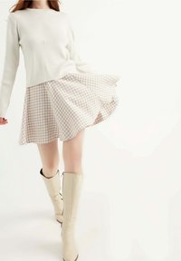 Bílý žebrovaný svetr doplněný béžovou a bílou sukní ve vzoru houndstooth se širokými nohavicemi; modelka má na sobě béžové kozačky po kolena.