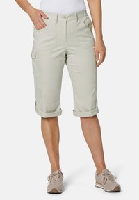 Beige knielange cargoshorts met opgerolde manchetten, meerdere voorzakken en een gladde stoftextuur. Gepaard met lichte sneakers.