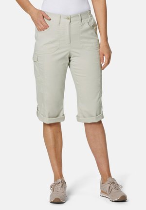 Shorts cargo beiges à mi-cuisses avec des revers, plusieurs poches avant et une texture de tissu lisse. Portés avec des baskets légères.