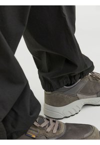 Svarta elastiska byxor med fåll, kombinerade med grå sneakers med en strukturerad ovandel, ljusgrå sula och framträdande snörning.