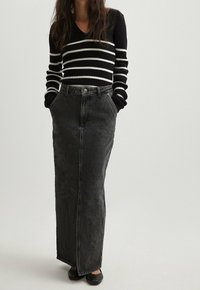 Gestreifter, schwarz-weißer Ripp-Pullover mit V-Ausschnitt, getragen mit einem langen, dunkelgrauen Jeansrock mit hoher Taille und seitlichen Taschen.