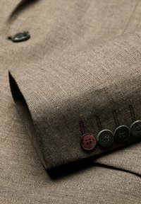 Braunes Leinenärmels mit sichtbarer Textur, ausgestattet mit fünf Knöpfen in unterschiedlichen Farben und einem dekorativen Stichmuster.
