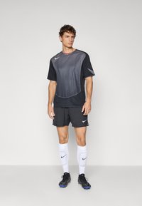 Black and gray athletic shirt with textured design, paired with black shorts, white socks, and black soccer cleats. Features Nike logos.