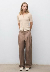 Cardigan bej cu dungi, cu mâneci scurte, închis cu nasturi, asortat cu pantaloni maro cu talie înaltă și pliuri, și pantofi de culoare deschisă.