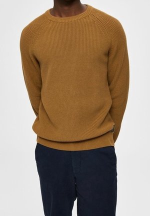 Bruine geribbelde gebreide trui met een ronde hals en raglanmouwen, gecombineerd met donkerblauwe broek van een gestructureerde stof.