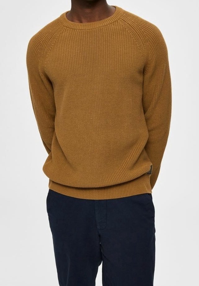 Hnědý žebrovaný pletený svetr s kulatým výstřihem a raglánovými rukávy, v kombinaci s tmavě modrými kalhotami s texturovaným materiálem.