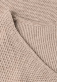 Gros plan sur un tissu tricoté côtelé beige montrant des bords pliés et un détail de couture texturé.