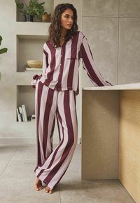 Knopf-Pyjama-Set mit breiten scharlachroten und helllila Streifen. Mit langen Ärmeln, Brusttasche und locker sitzenden Hosen mit weitem Bein.