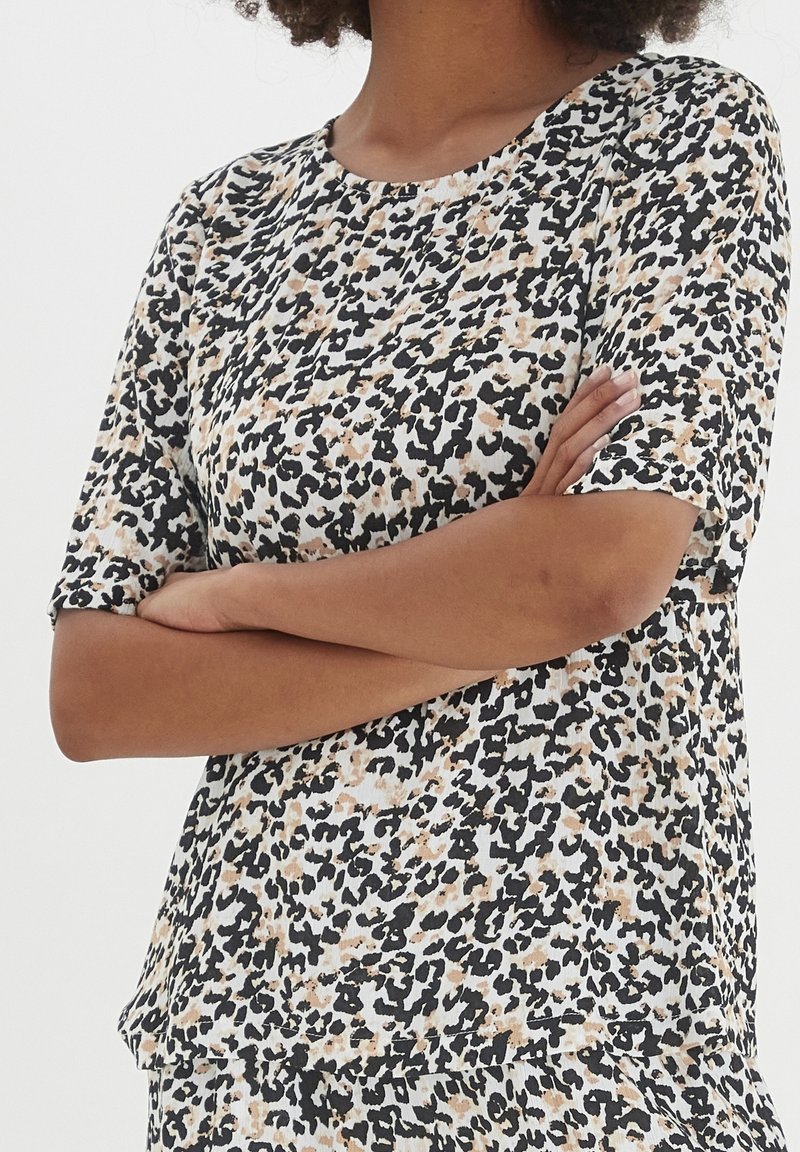 Top a maniche corte con motivo leopardato, in colori nero, beige e bianco. Realizzato in tessuto morbido con una vestibilità comoda.
