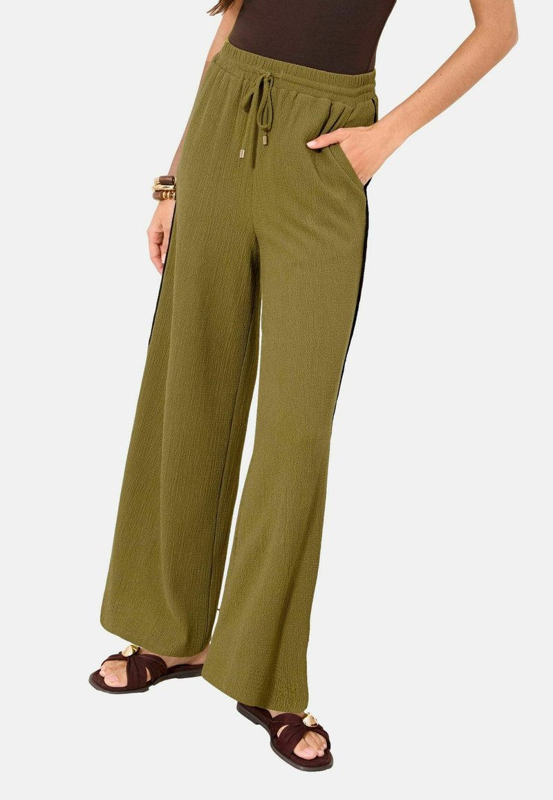 Femme portant un pantalon large couleur olive avec taille à cordon et poches latérales, assorti à des sandales foncées et un haut marron.