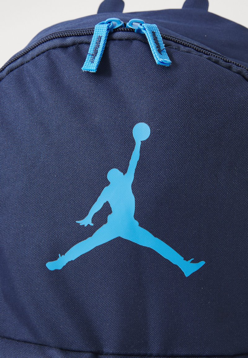 Silueta azul de un jugador de baloncesto saltando con un brazo levantado sosteniendo una pelota sobre una superficie de tela azul oscura con dos tiradores de cremallera azules.