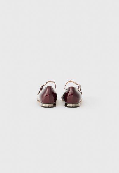 Sapatos de couro patente bordô com uma tira traseira, pequenos detalhes em prata e um design de bico arredondado. Sola plana e acabamento suave.